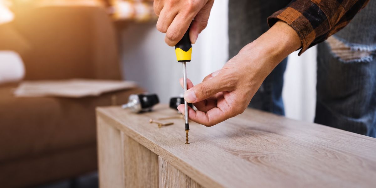 Hands driving a screw into a wooden cabinet with a screwdriver